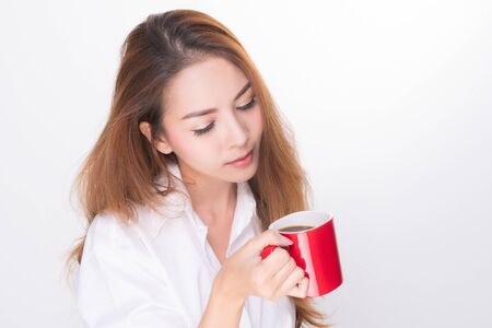 Asian woman portrait with perfect skin and wearing a white shirt in happiness holding red coffee cup isolated on white background.の写真素材