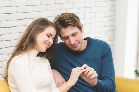 European couples, caucasian man wearing blue sweater and woman wearing white sweater hugging and holding hands while looks an engagement ring in the room.の写真素材