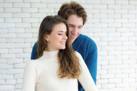 European couples, caucasian man wearing blue sweater and woman wearing white sweater, are standing happily hugging each other in the room.の写真素材