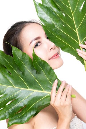 Close-up studio shot, Beautiful young woman with clean fresh skin holding green leaves. Proposing a product. Gestures for advertisement isolated on white background.の写真素材