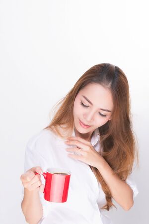 Asian woman portrait with perfect skin and wearing a white shirt in happiness holding red coffee cup isolated on white background.の写真素材