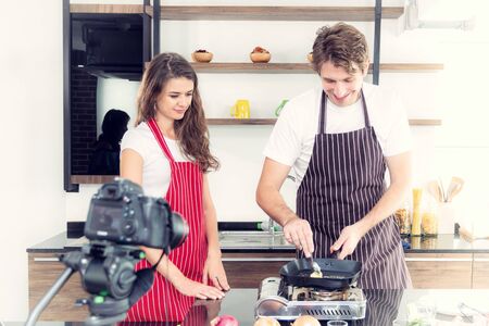 Vlogger and blogger freelance job concept, Young couple cooking together and recording live video for her vlog and social media with camera and tripodの写真素材