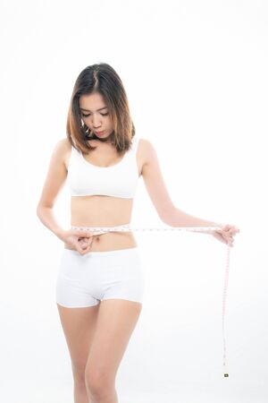Young beautiful brunette woman wearing white underwear showing the measurements using measure tape at studio shoot isolated on white backgroundの写真素材