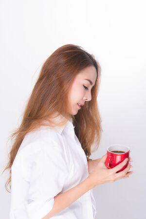Asian woman portrait with perfect skin and wearing a white shirt in happiness holding red coffee cup isolated on white background.の写真素材