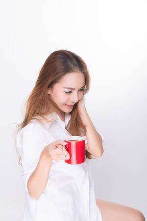Asian woman portrait with perfect skin and wearing a white shirt in happiness holding red coffee cup isolated on white background.の写真素材