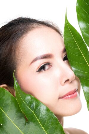 Close-up studio shot, Beautiful young woman with clean fresh skin holding green leaves. Proposing a product. Gestures for advertisement isolated on white background.の写真素材