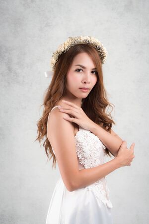 Vintage style portrait beautiful woman wearing a white dress, flower crown on gray soft blurred background.の写真素材