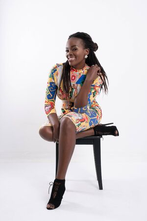 Beautiful African woman hair dreadlocks with a happy posture wearing a flower-patterned dress, wearing black high-heeled shoes, wearing earrings full length body portrait isolated on white background.の写真素材