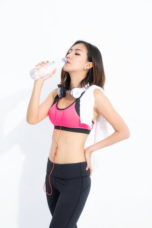 Sporty girl eating water with towel on her shoulders.  Photo of fitness model isolated on white background. Sport and healthy lifestyle.の写真素材
