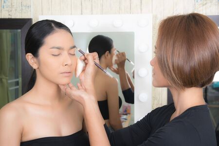 Young beautiful asian woman applying makeup by makeup artist on location.の写真素材