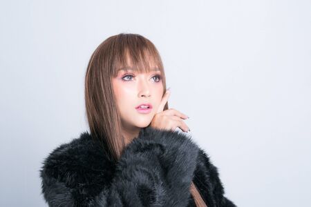 Beautiful asian model posing in a fur coat is fashion photography at studio lighting shoot isolated on gray background.の写真素材