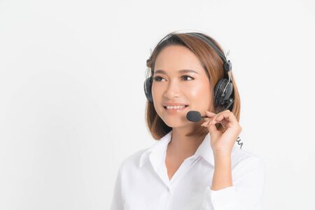 Portrait of happy smiling female customer support phone operator short hair, wearing a white shirt with headset standing one side holding the earphone isolated on white background.の写真素材