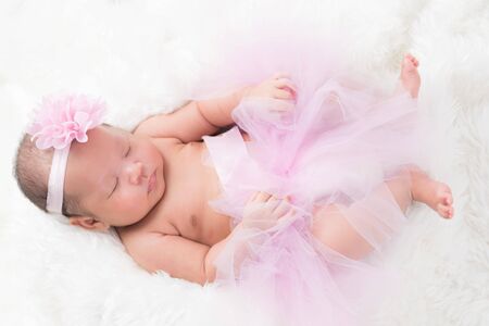 Cute newborn baby wears a pink flower crown lies swaddled in a white blanket.の写真素材