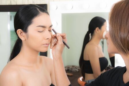 Young beautiful asian woman applying makeup by makeup artist on location.の写真素材
