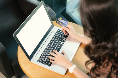 Hand woman holding credit card and using laptop with white screen within the coffee shop. Shopping...