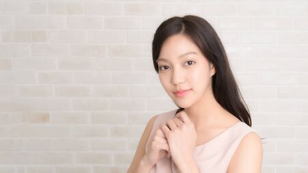 Close up, Beautiful asian pretty woman long brown hair smiling and facing her side view with wearing a black t-shirt and jeans standing positng on beige color wall.の写真素材