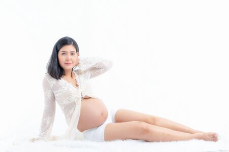 Studio fashion portrait pregnant happy woman. Pregnant young mother portrait, caressing her belly and smiling close-up. Healthy Pregnancy concept at white room. Sit position.の写真素材