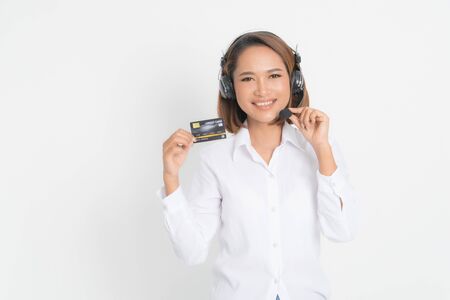 Friendly female helpline operator or call center showing blank credit card, headset holding her arms crossed isolated on white background.の写真素材