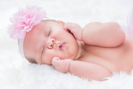 Cute newborn baby wears a pink flower crown lies swaddled in a white blanket.の写真素材