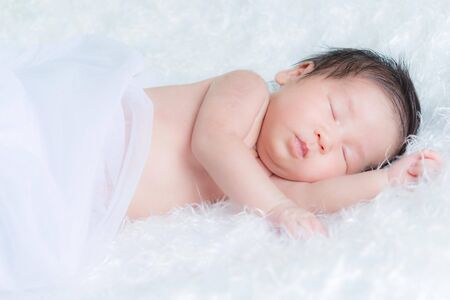 Cute baby on newborn is yawning on a white fluffy fur. Fashion baby portrait concept.の写真素材