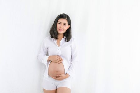 Pregnant happy Woman touching her belly. Pregnant young mother portrait, caressing her belly and smiling close-up. Healthy Pregnancy concept, brunette expectant female isolated on white background.の写真素材