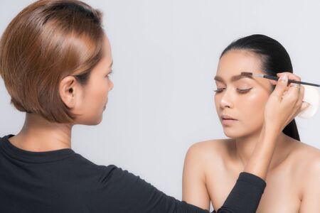 Young beautiful asian woman applying makeup by makeup artist on location.の写真素材