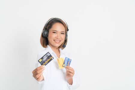 Friendly female helpline operator or call center showing blank credit card, headset holding her arms crossed isolated on white background.の写真素材