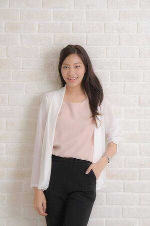 Beautiful asian pretty woman long brown hair smiling and facing her side view with wearing a black t-shirt and jeans standing positng on beige color wall.の写真素材