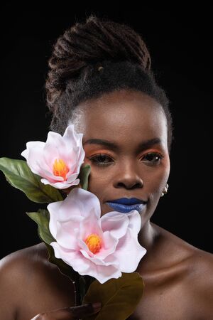 Close up, Beautiful woman model african woman with orange makeup on her eyes. Concept colourful makeup with flower. Studio shot isolated black background.の写真素材