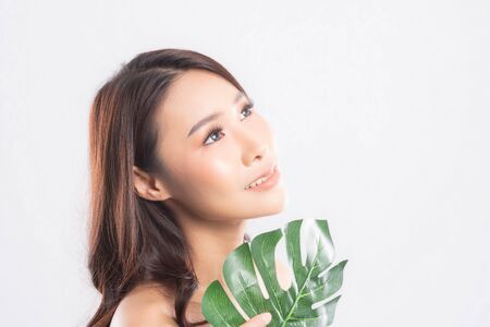 Close-up studio shot, Beautiful young woman with clean fresh skin holding green leaves. Proposing a product. Gestures for advertisement isolated on white background.の写真素材