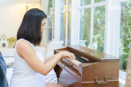 Pregnant woman playing the piano by the window in the bedroom.の写真素材