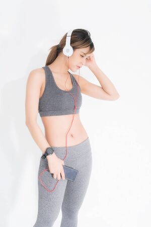 Fitness woman listening to music wearing white music headphones, enjoys sports and healthy lifestyle isolated on a white background. She is relaxing and happiness.の写真素材