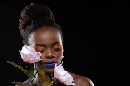 Close up, Beautiful woman model african woman with orange makeup on her eyes. Concept colourful makeup with flower. Studio shot isolated black background.の写真素材