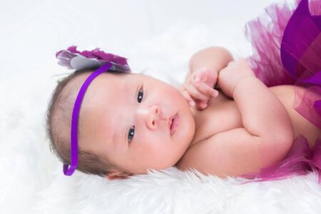 Cute newborn baby wears a magenta flower crown lies swaddled in a white blanket.の写真素材