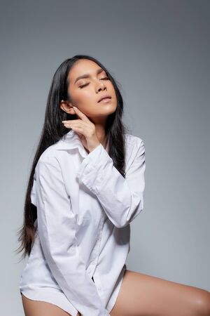 Asian woman portrait with perfect skin and wearing a white shirt in profile isolated on gray background.の写真素材