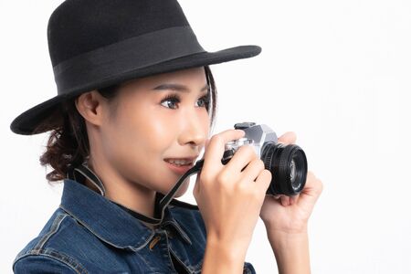 Beautiful female tourist wearing a black hat and jeans jacket is standing to take a picture with a vintage camera in happiness at studio shot isolated on white background.の写真素材