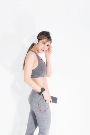 Fitness woman listening to music wearing white music headphones, enjoys sports and healthy lifestyle isolated on a white background. She is relaxing and happiness.の写真素材