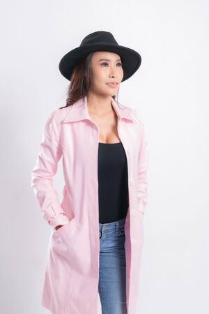 Young elegant woman in trendy pink coat wearing a black hat, at fashion studio portrait shot isolated on white background.の写真素材