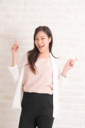 Beautiful asian pretty woman long brown hair smiling and facing her side view with wearing a black t-shirt and jeans standing positng on beige color wall.の写真素材