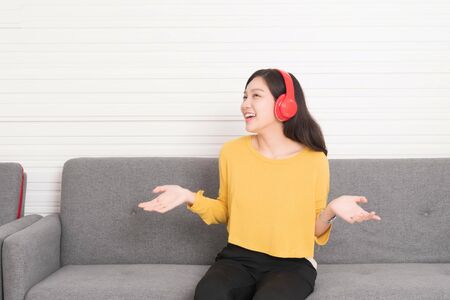 Beautiful asian woman long hair wearing a yellow shirt with red headphones relaxing on the sofa, she is listening to music, chill out and leisure concept.の写真素材