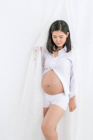 Pregnant happy Woman touching her belly. Pregnant young mother portrait, caressing her belly and smiling close-up. Healthy Pregnancy concept, brunette expectant female isolated on white background.の写真素材