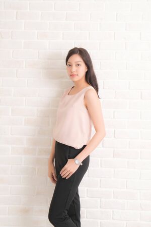Beautiful asian pretty woman long brown hair smiling and facing her side view with wearing a black t-shirt and jeans standing positng on beige color wall.の写真素材