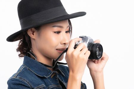 Beautiful female tourist wearing a black hat and jeans jacket is standing to take a picture with a vintage camera in happiness at studio shot isolated on white background.の写真素材