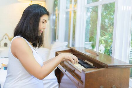 Pregnant woman playing the piano by the window in the bedroom.の写真素材