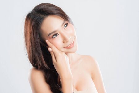 Beautiful young woman with clean fresh skin, Hair sleek, Proposing a product. Gestures for advertisement on gray background, Front view, with copy space.の写真素材