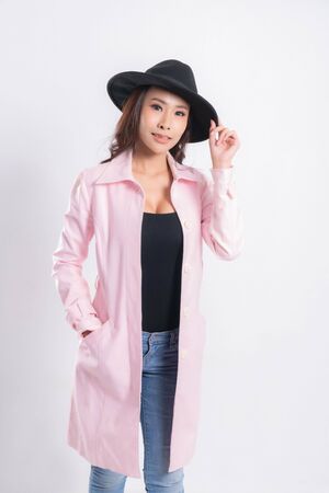 Young elegant woman in trendy pink coat wearing a black hat, at fashion studio portrait shot isolated on white background.の写真素材