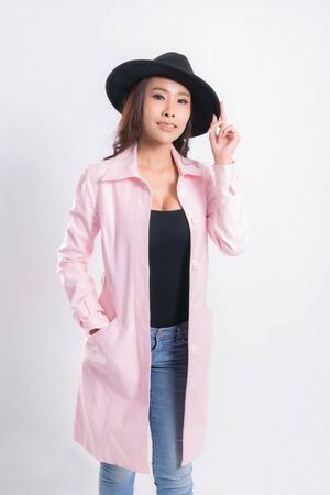 Young elegant woman in trendy pink coat wearing a black hat, at fashion studio portrait shot isolated on white background.の写真素材