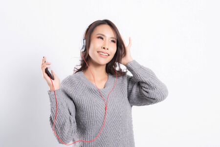 Young beautiful woman wearing a gray sweater is lying and listening to music wearing white music headphones isolated on white background. She is relaxing and happinessの写真素材