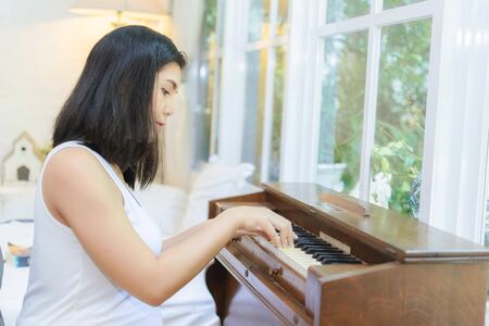 Pregnant woman playing the piano by the window in the bedroom.の写真素材