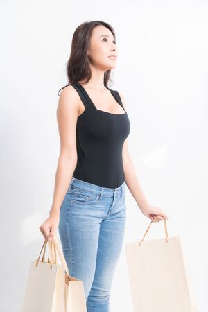 Happy beautiful asian woman black long-haired woman wearing a black shirt, blue jeans carrying shopping bags  on isolated gray background, Shopping summer sale concept.の写真素材